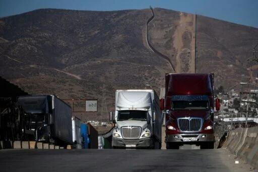 Cargo trucks queue next to the border wall before crossing into Tijuana ...